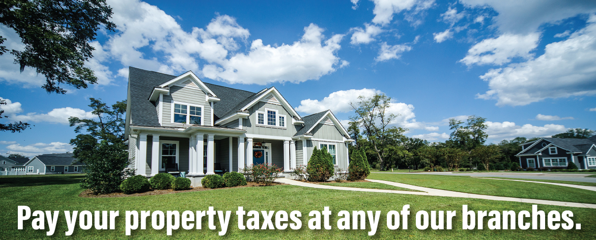 Modern house with green lawn and text encouraging property tax payment at bank locations.